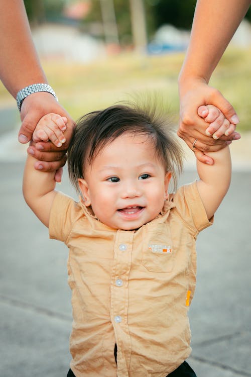 Free A baby holding onto the hands of two adults Stock Photo