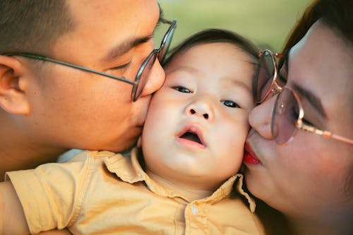 Free A man and woman kiss a baby while wearing glasses Stock Photo