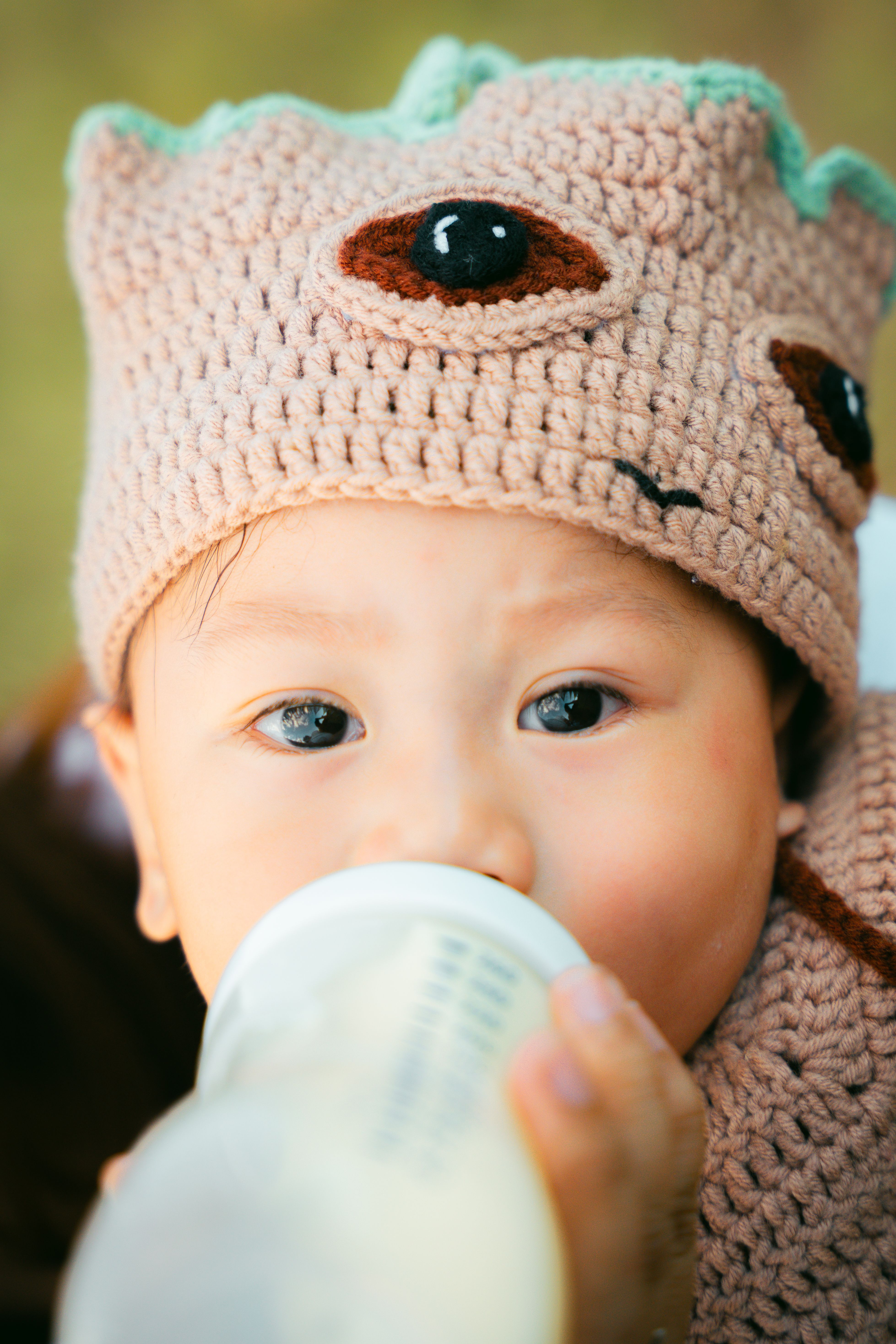 Close-up of a child with a whimsical knit hat drinking milk from a bottle.