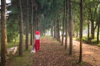 一位红衣女子走在树木繁茂的小路上，四周环绕着高大的树木