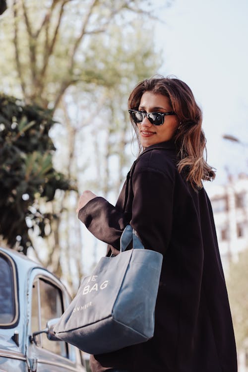 A woman in sunglasses holding a blue tote bag