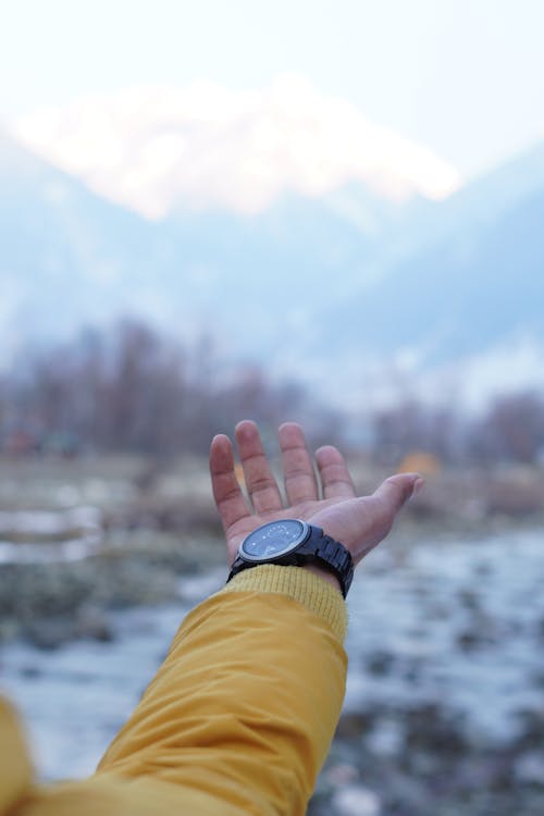Free A person holding up their wrist with mountains in the background Stock Photo