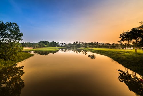 Água Calma Cercada Por Um Campo De Grama Verde Durante O Pôr Do Sol