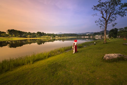 日落时分，一名戴红帽子的女子站在宁静的湖边，捕捉着这份宁静