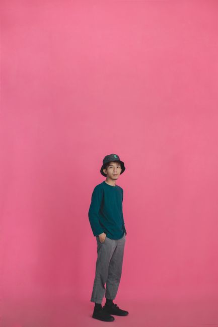 Confident young boy in modern outfit posing against a vibrant pink backdrop.