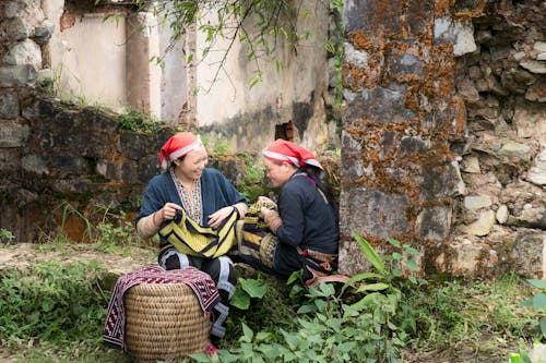 Photo of Two Women Sitting Beside Wall