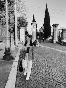 A stylish young woman walks along a cobblestone street in a timeless black and white setting.