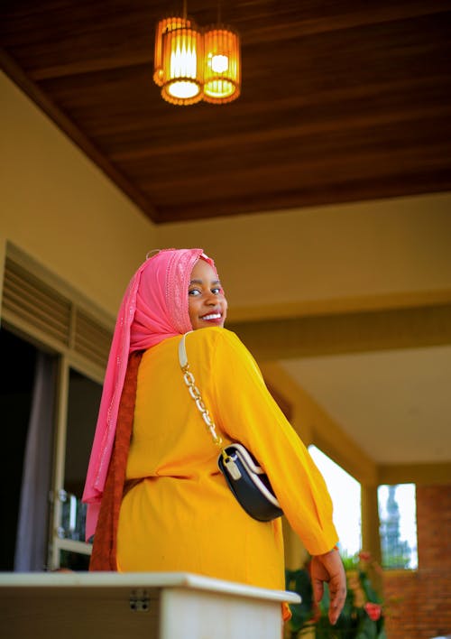 Free A Young Woman Wearing a Yellow Dress and a Pink Headscarf Looking over Her Shoulder  Stock Photo