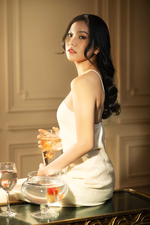 A woman in a white dress sitting on a table with a glass of wine