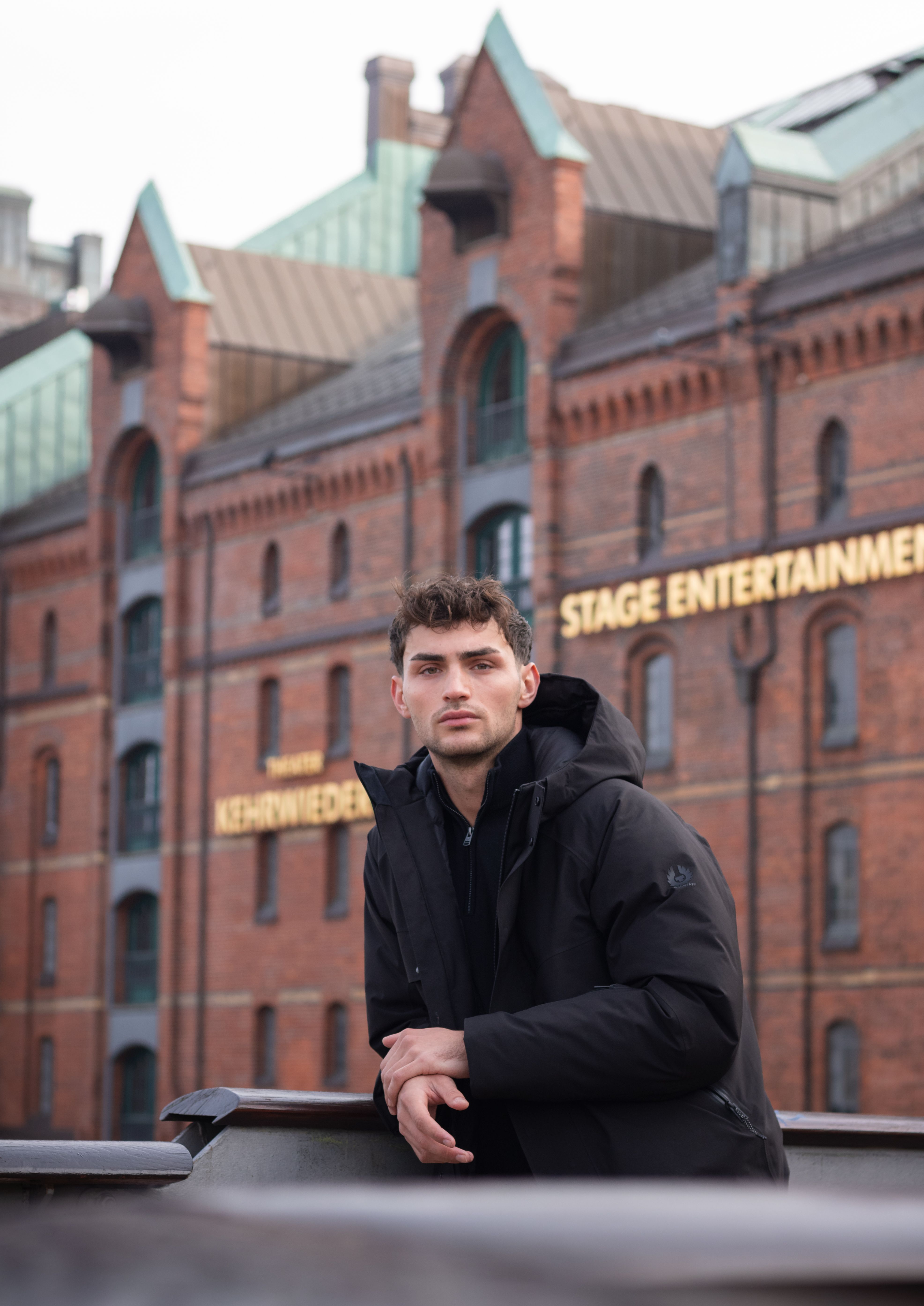 Fashionable young man in black jacket poses at iconic Hamburg Speicherstadt.