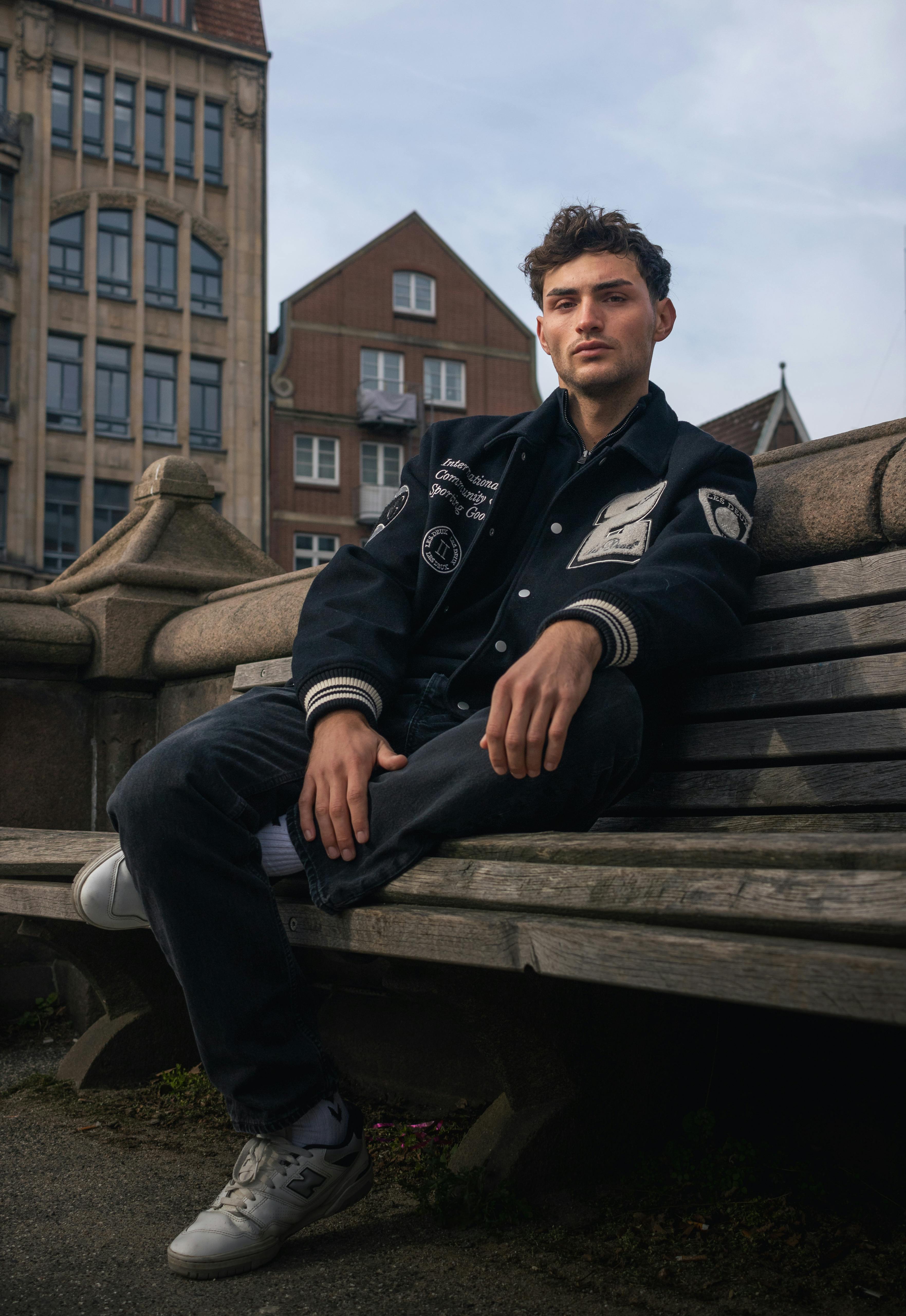 Caucasian man in sports jacket posing on a bench in Hamburg's urban setting.