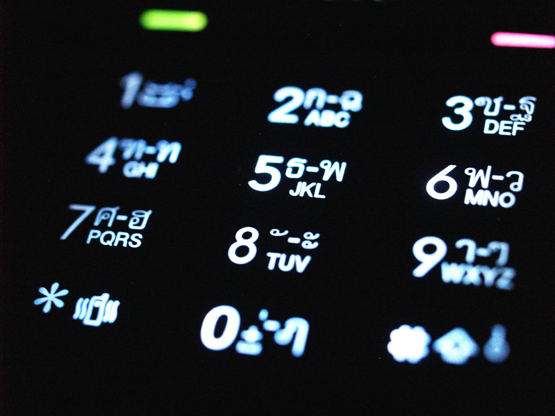 Close-up view of an illuminated mobile phone keypad displaying numbers and Thai script in a dark setting.