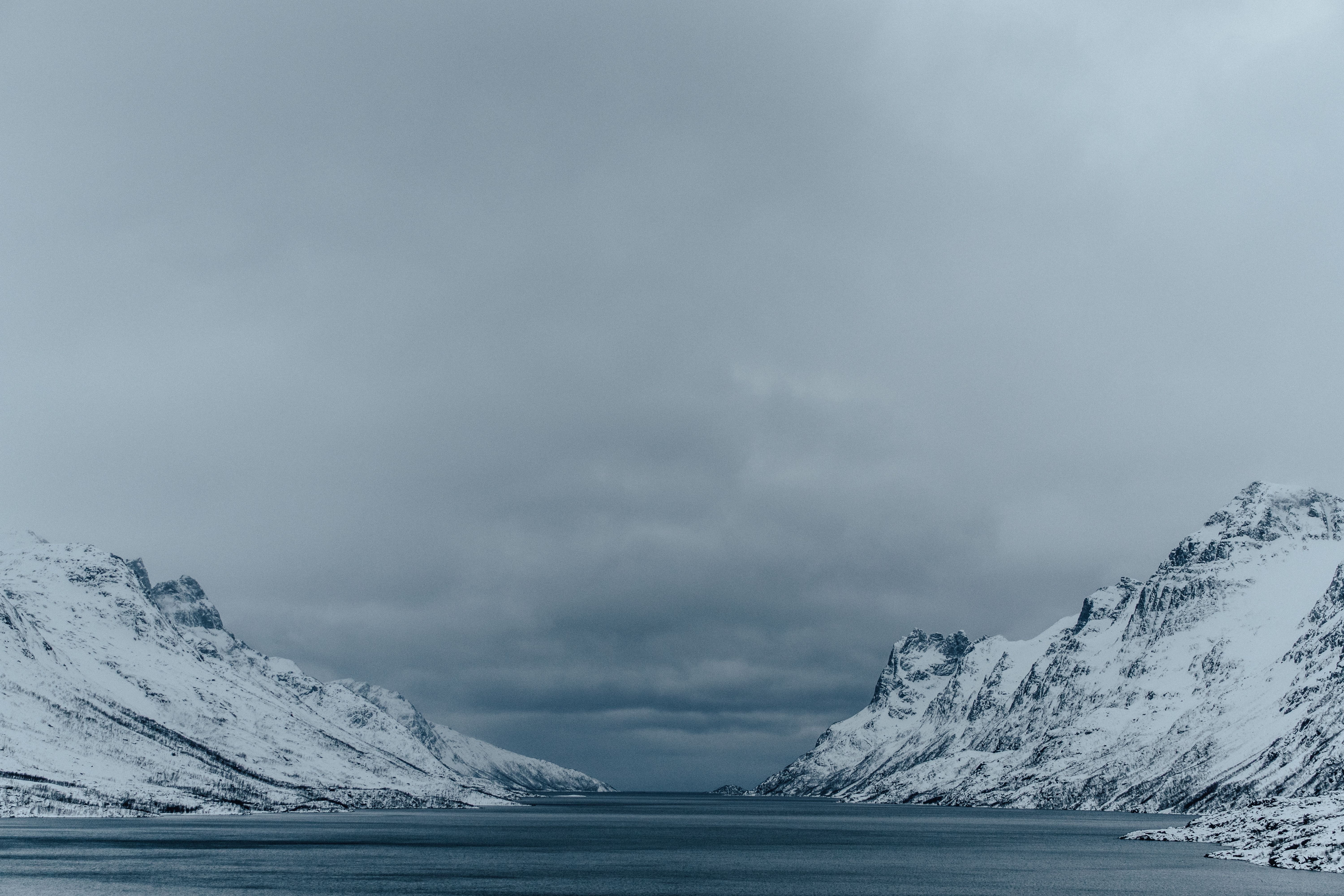 Peaceful winter landscape with snowy mountains and a calm lake under a cloudy sky.