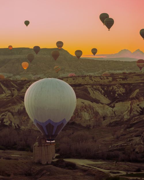 Free Stunning view of hot air balloons floating over Cappadocia's unique landscape during a vibrant sunset. Stock Photo