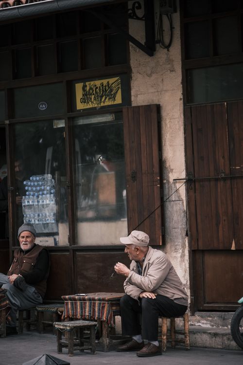 Free Two senior men sit and talk outside a rustic urban store, enjoying a peaceful day. Stock Photo