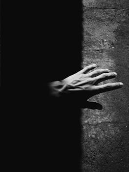 这是一张高对比度的单色图像，描绘了一只手从黑暗进入光明的瞬间