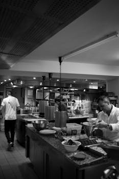 Black and white photo capturing chefs preparing dishes in a vibrant restaurant kitchen.