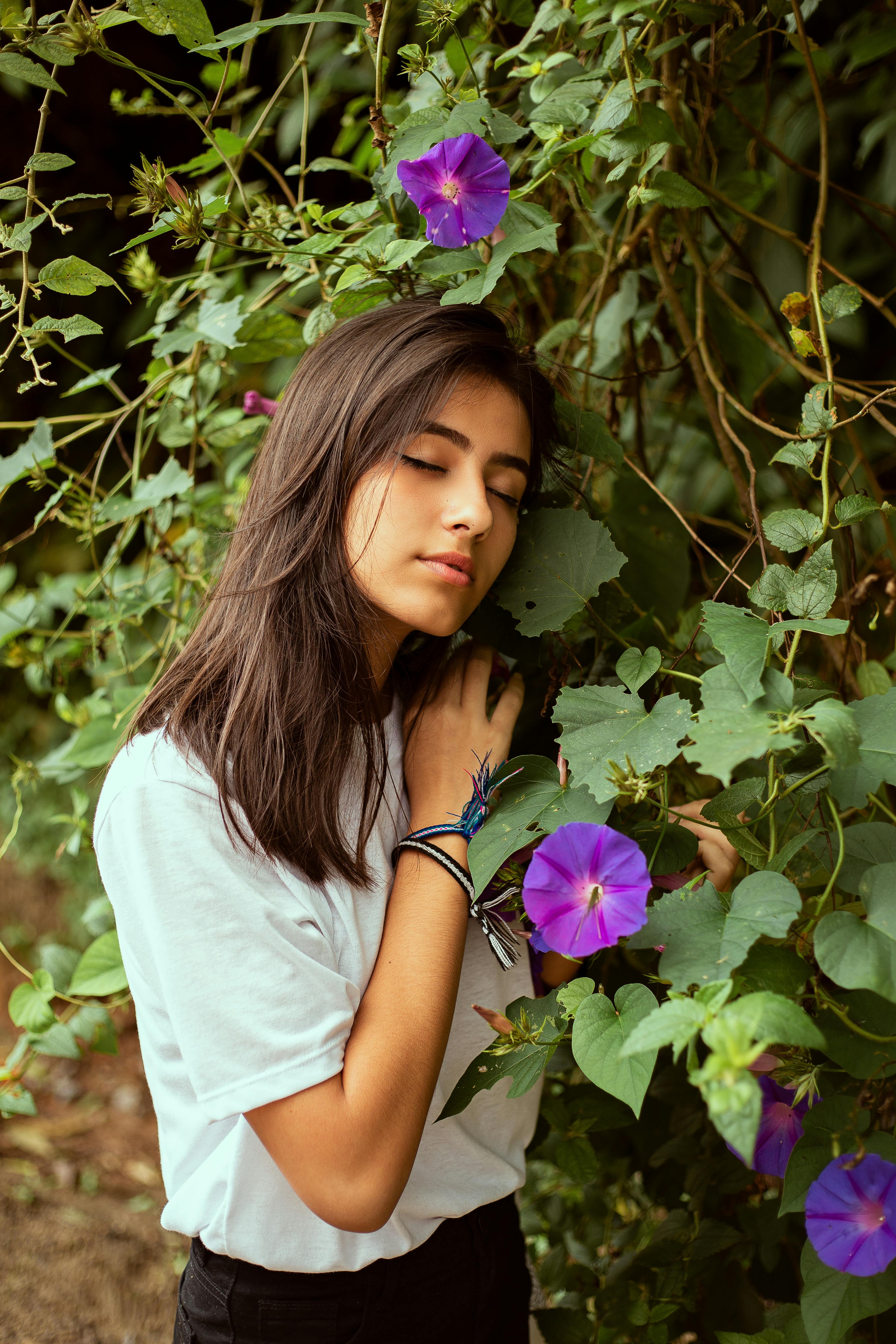 一名女子闭着眼睛，沐浴在户外生机勃勃的紫色牵牛花丛中