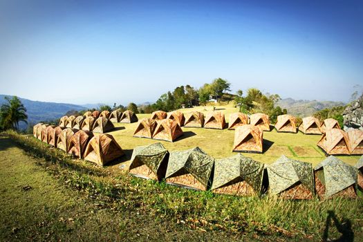 Idyllic campsite with multiple tents on a green mountain clearing under a clear blue sky.