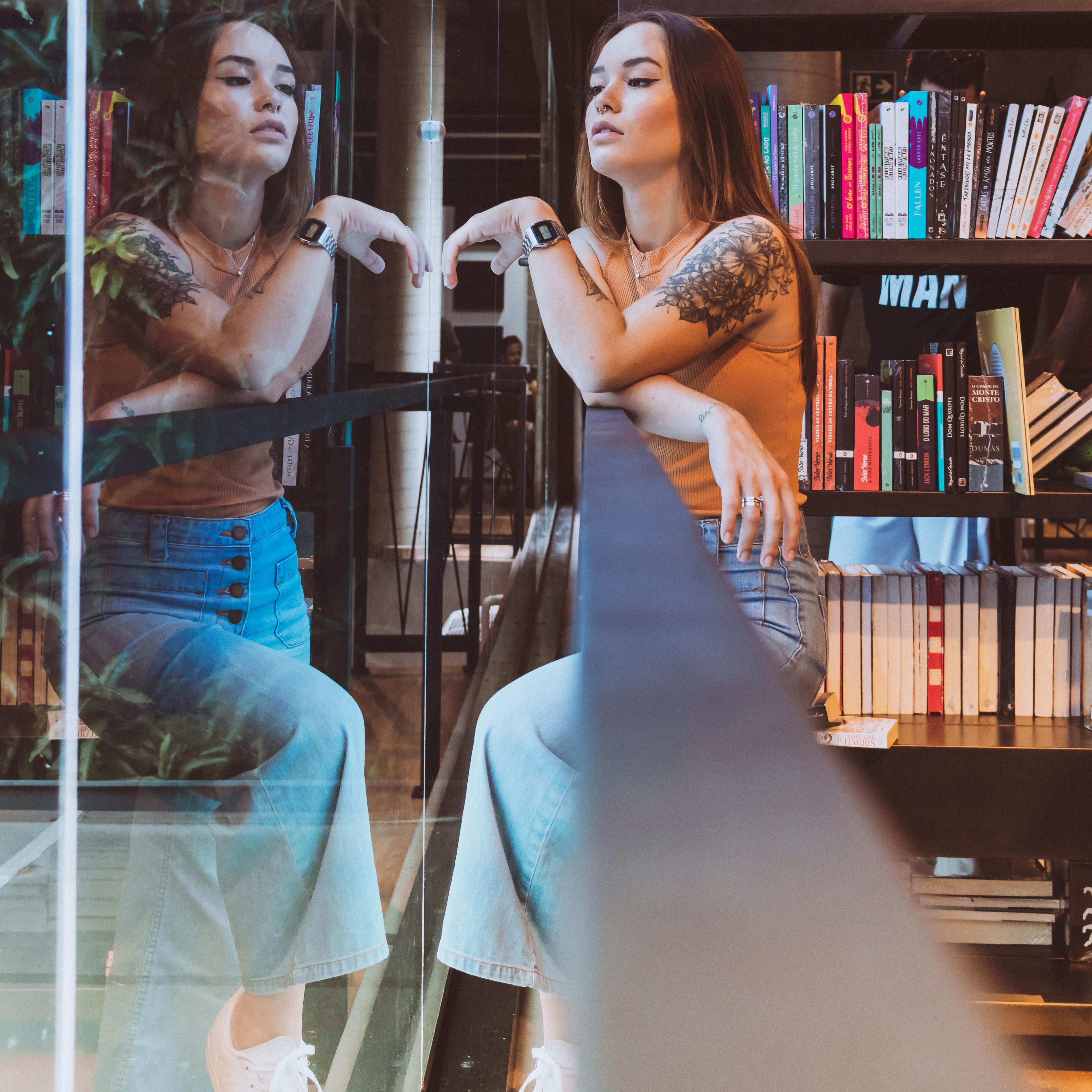 现代图书馆里，一位时尚女性倒映其中，四周环绕着书籍，纹身艺术清晰可见