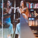现代图书馆里，一位时尚女性倒映其中，四周环绕着书籍，纹身艺术清晰可见