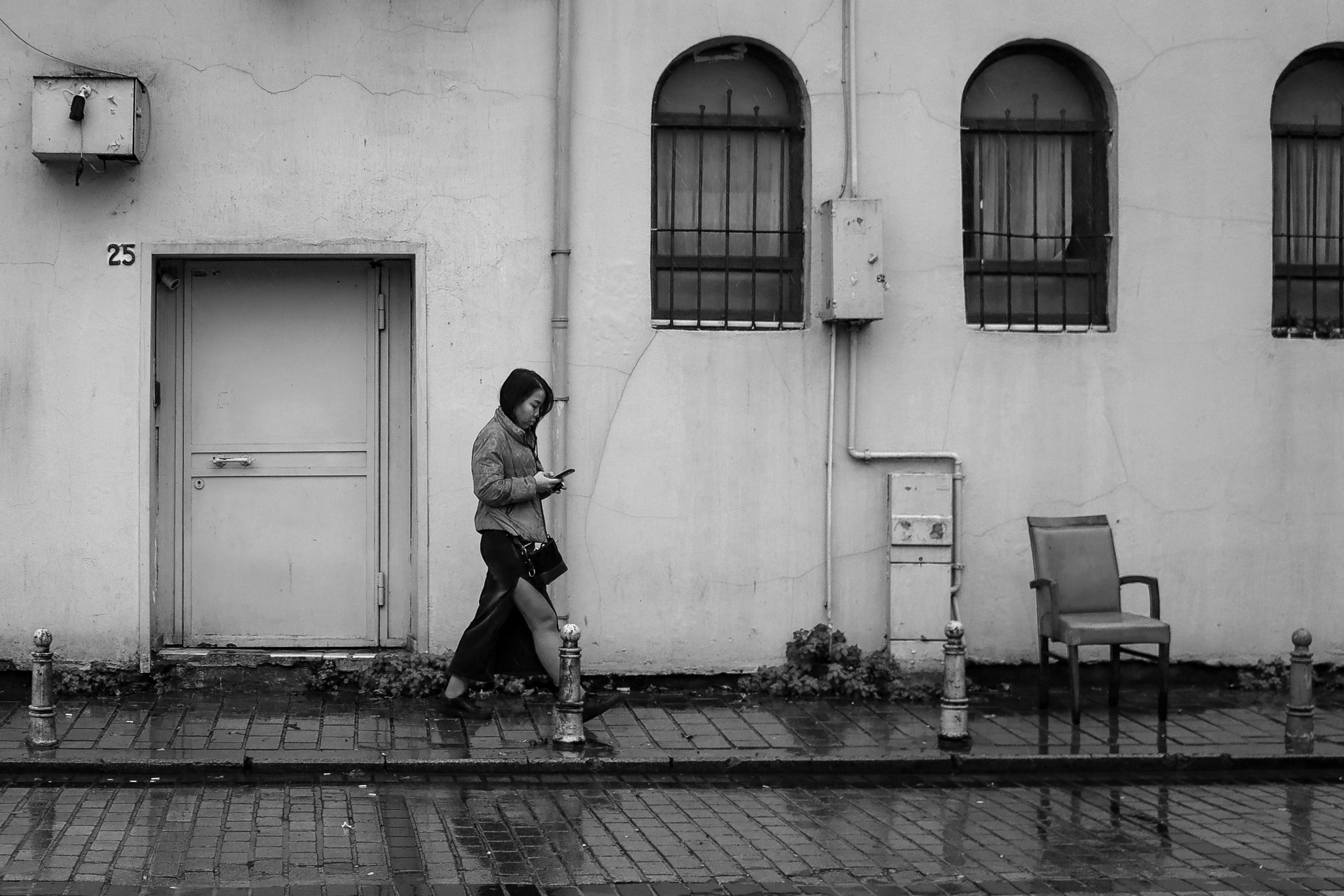 black and white photography of a young woman walking and looking at her smartphone