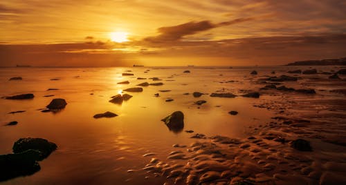 A sunset over the ocean with rocks and sand