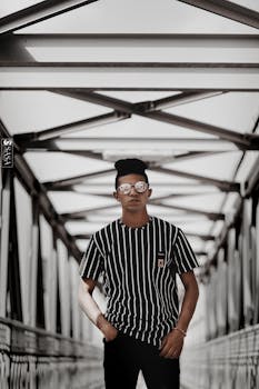 一位戴着太阳镜和条纹衬衫的时尚男子坐在现代金属桥上