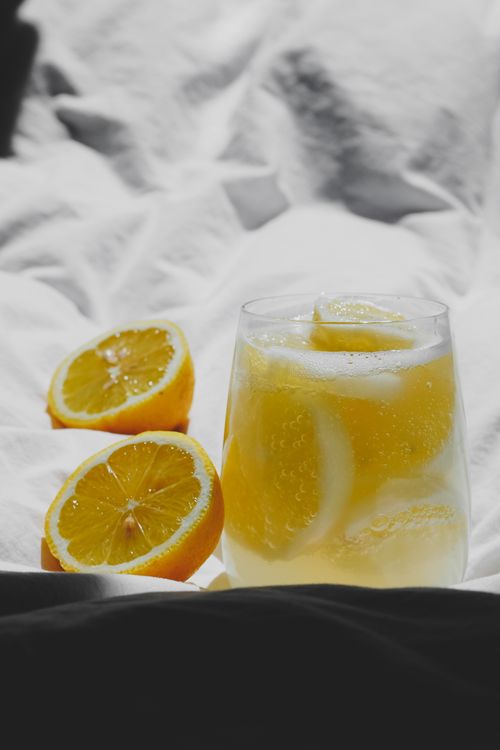 Free Glass of refreshing lemonade with sliced lemons on soft white bedding, evoking a fresh and citrusy feel. Stock Photo