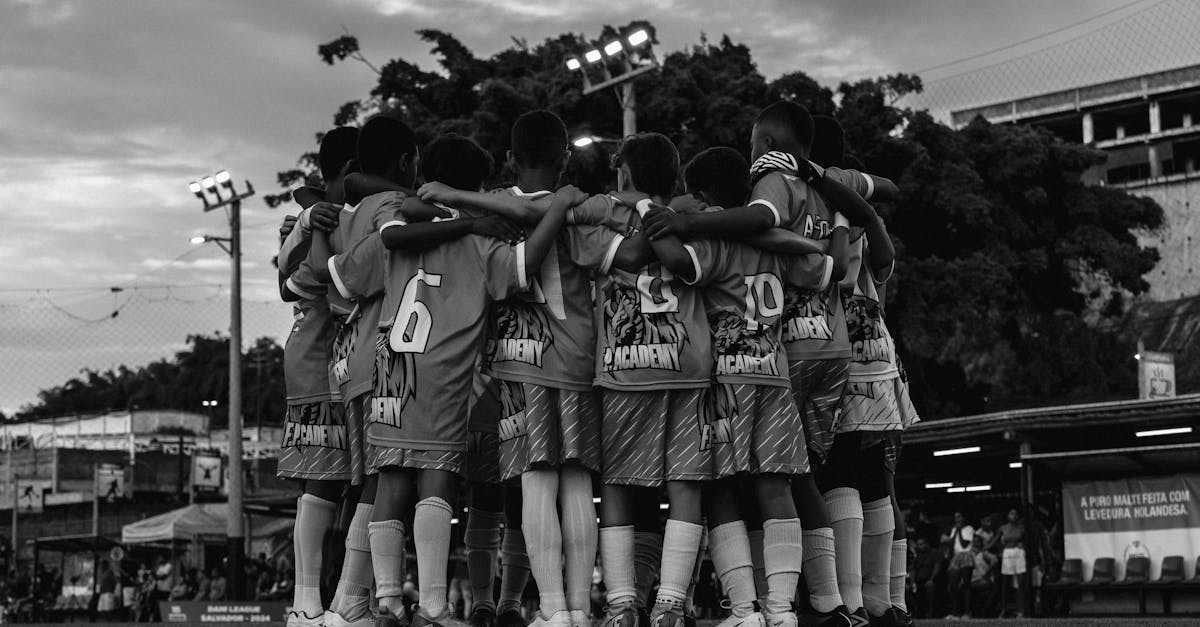 A black and white photo of a youth soccer team huddling on the field during dusk.