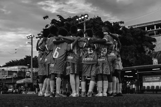 Group of young soccer players huddling before a match at an outdoor stadium.