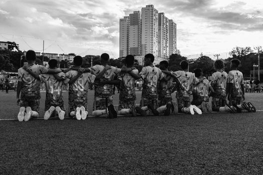 A black and white photo of a soccer team kneeling and embracing on a field with a city backdrop.
