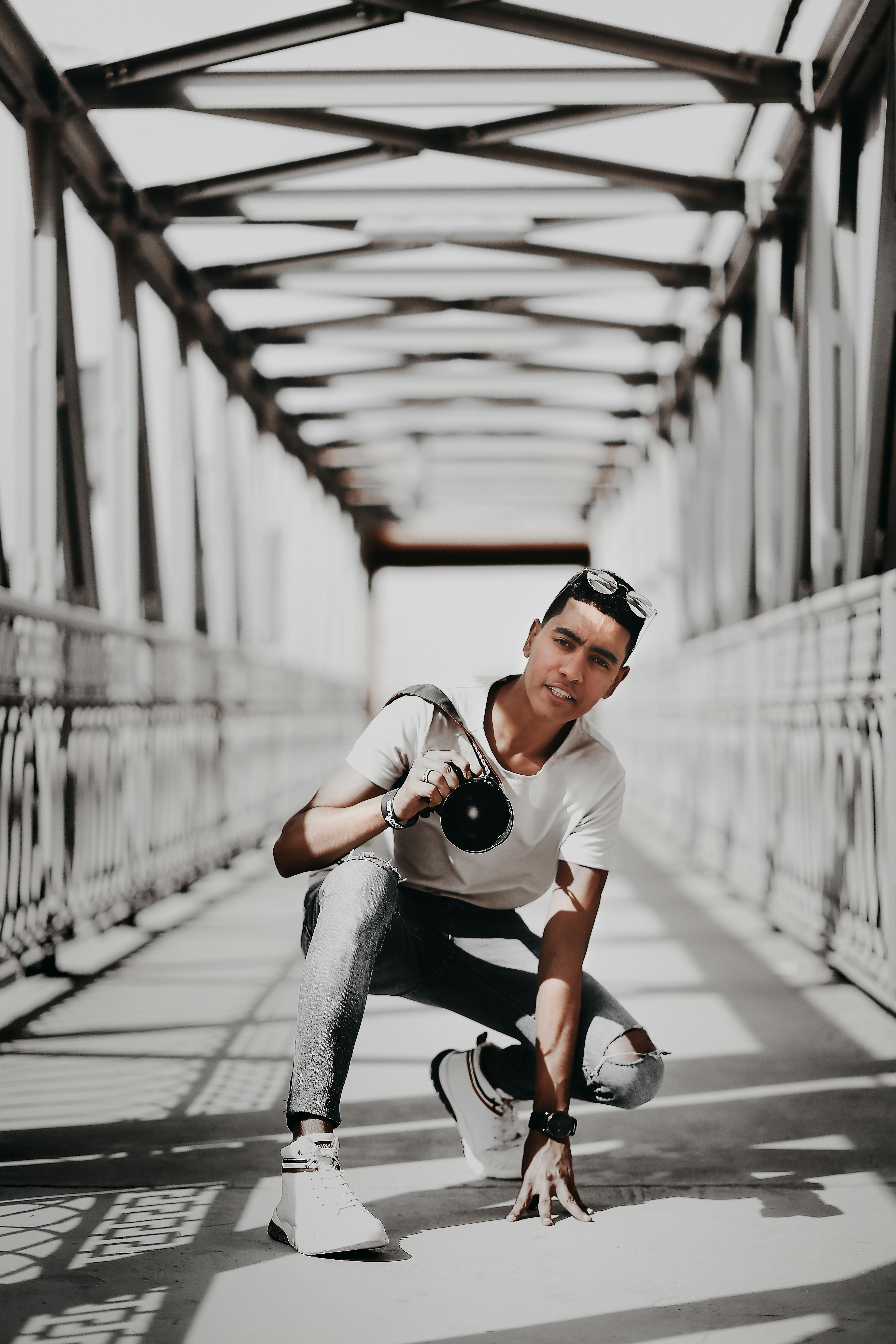 一位时尚的成年男性在现代风格的桥上手持相机摆姿势，展现都市时尚