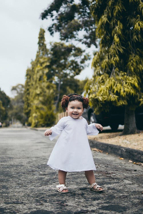 Smiling Baby Girl Wearing White Dress Standing on Road