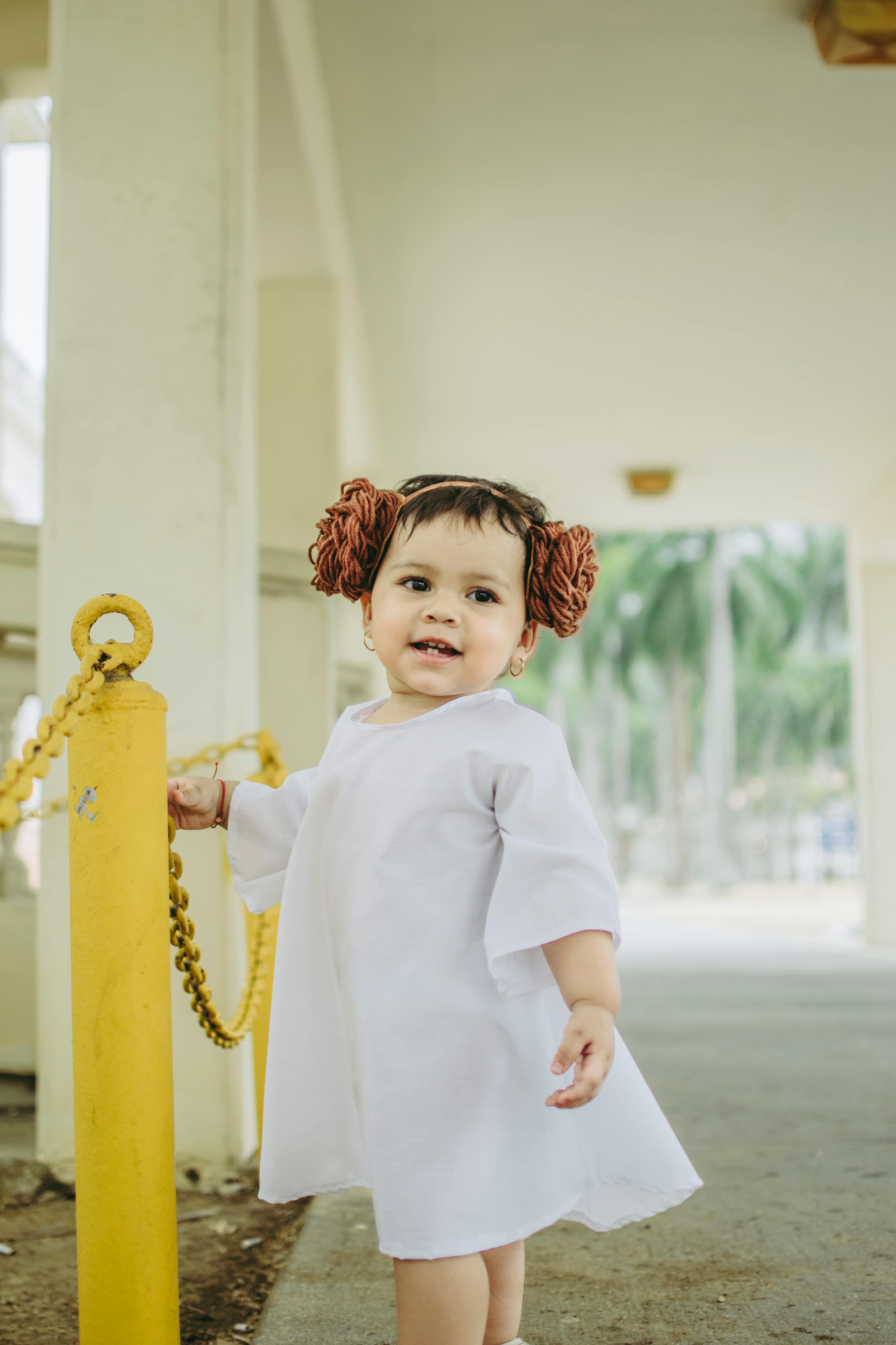 一个穿着白色连衣裙、头戴花发带的可爱宝宝在户外玩耍，欢乐的瞬间被捕捉下来