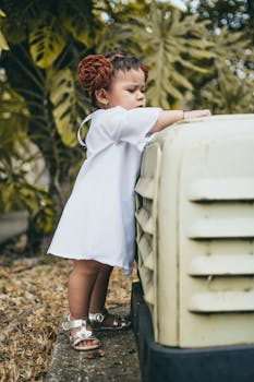 一个穿着白色连衣裙的可爱幼儿站在户外的大物体旁