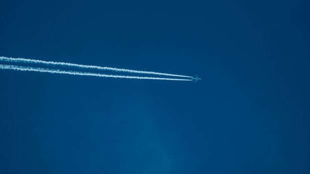 Jet flying high with contrails against a clear blue sky, showcasing aviation in action.