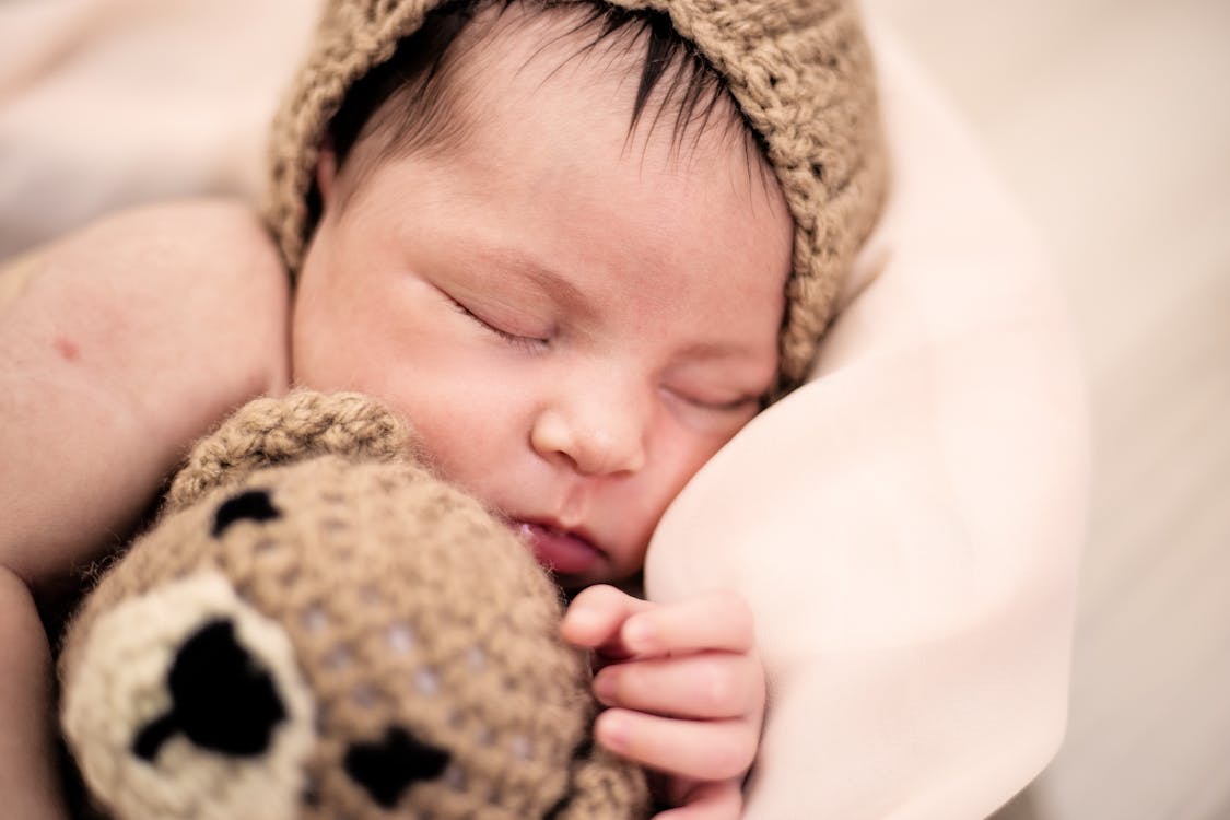 Baby sleeping soundly with a brown beanie and stuffed bear