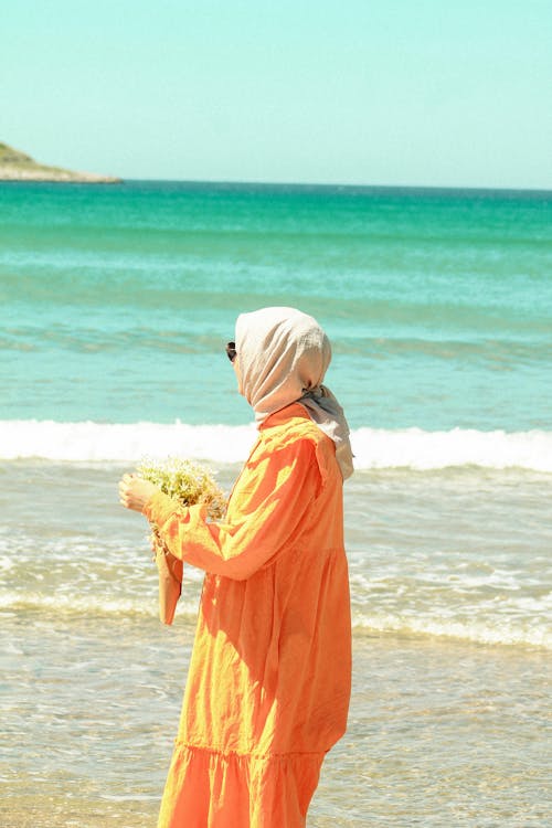 A woman in an orange dress is standing on the beach