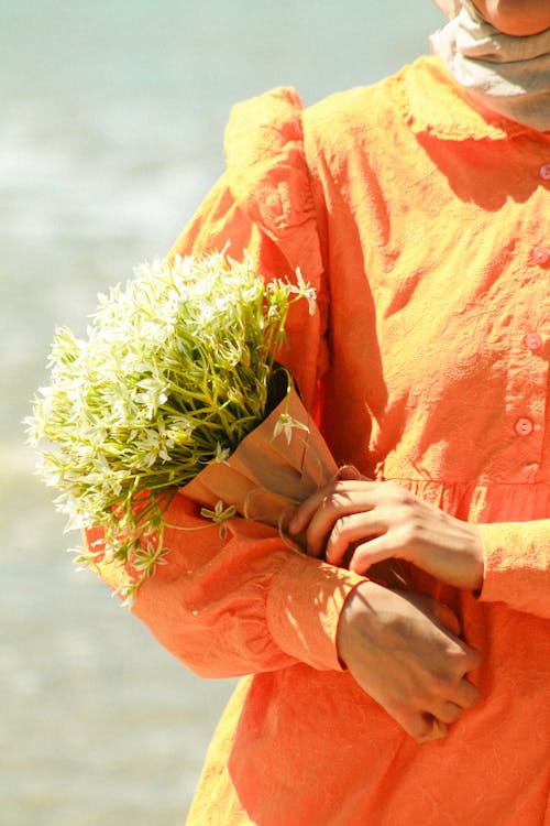 A woman in an orange shirt holding flowers by the beach