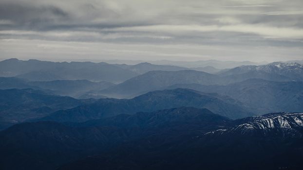 Stunning aerial view of the Andes mountain range in Mendoza, Argentina, showcasing vast peaks and cloudy skies.