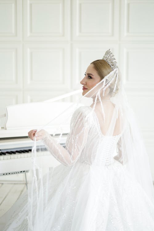 A woman in a wedding dress is posing near a piano