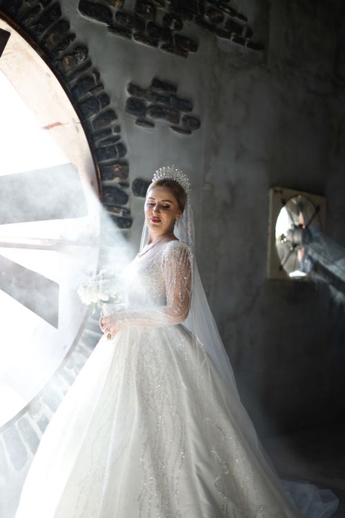 Free A beautiful bride in a white gown illuminated by sunlight in an industrial setting. Stock Photo