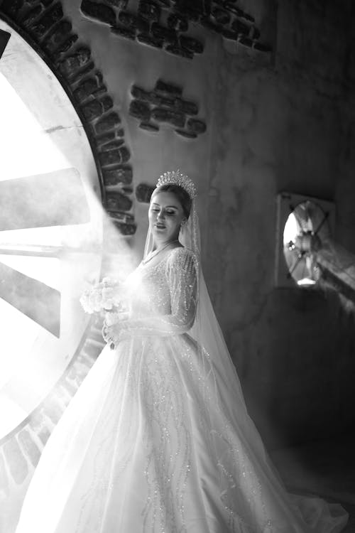 A bride in a wedding dress standing in front of a large circular window