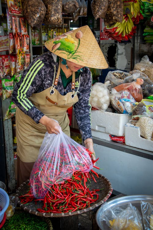 A woman in a hat and apron is sorting red peppers