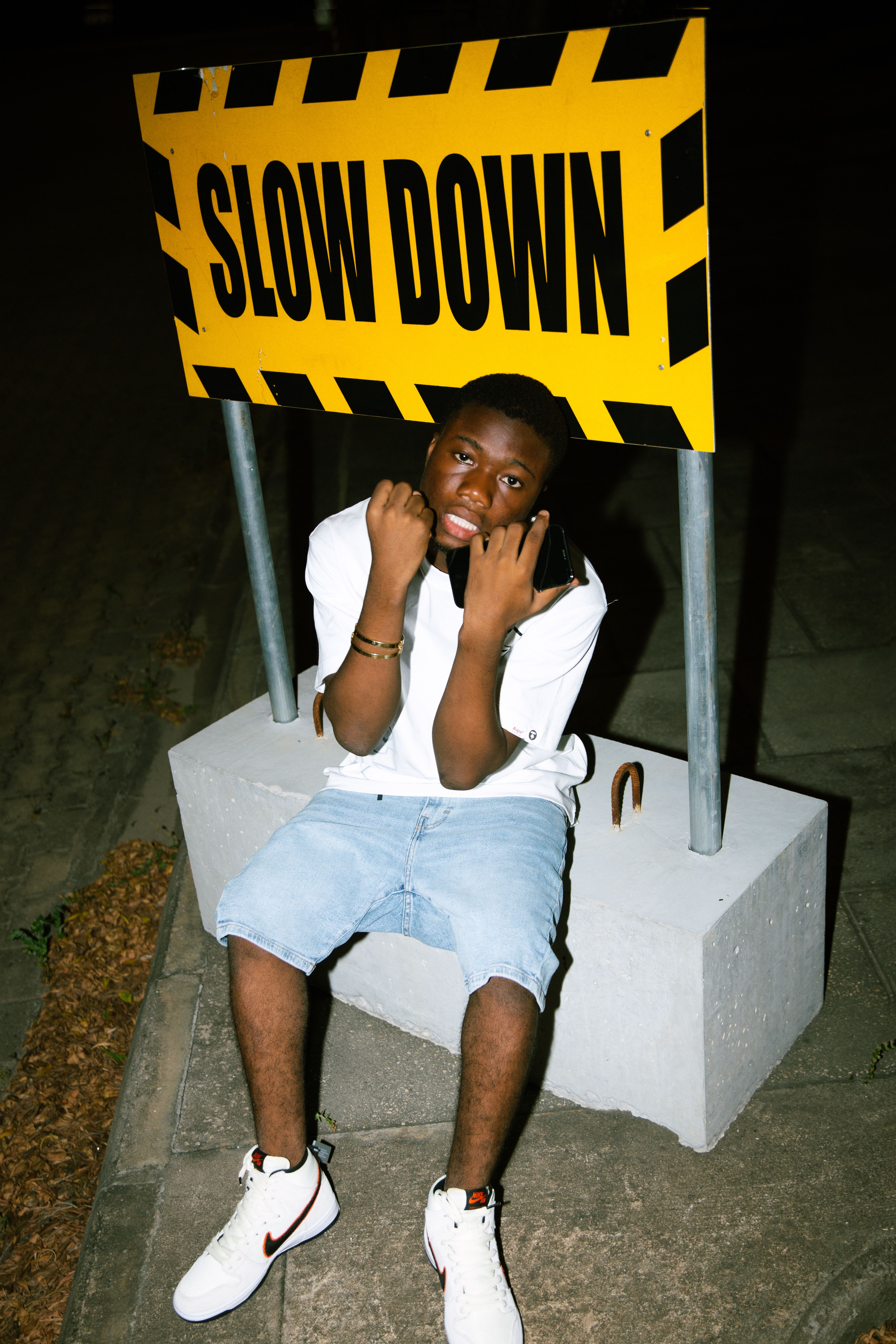 Teen in casual wear poses outdoors by a slow down road sign at night.