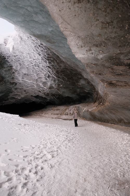 Free A lone figure stands inside a vast, stunning ice cave with textured icy walls. Stock Photo