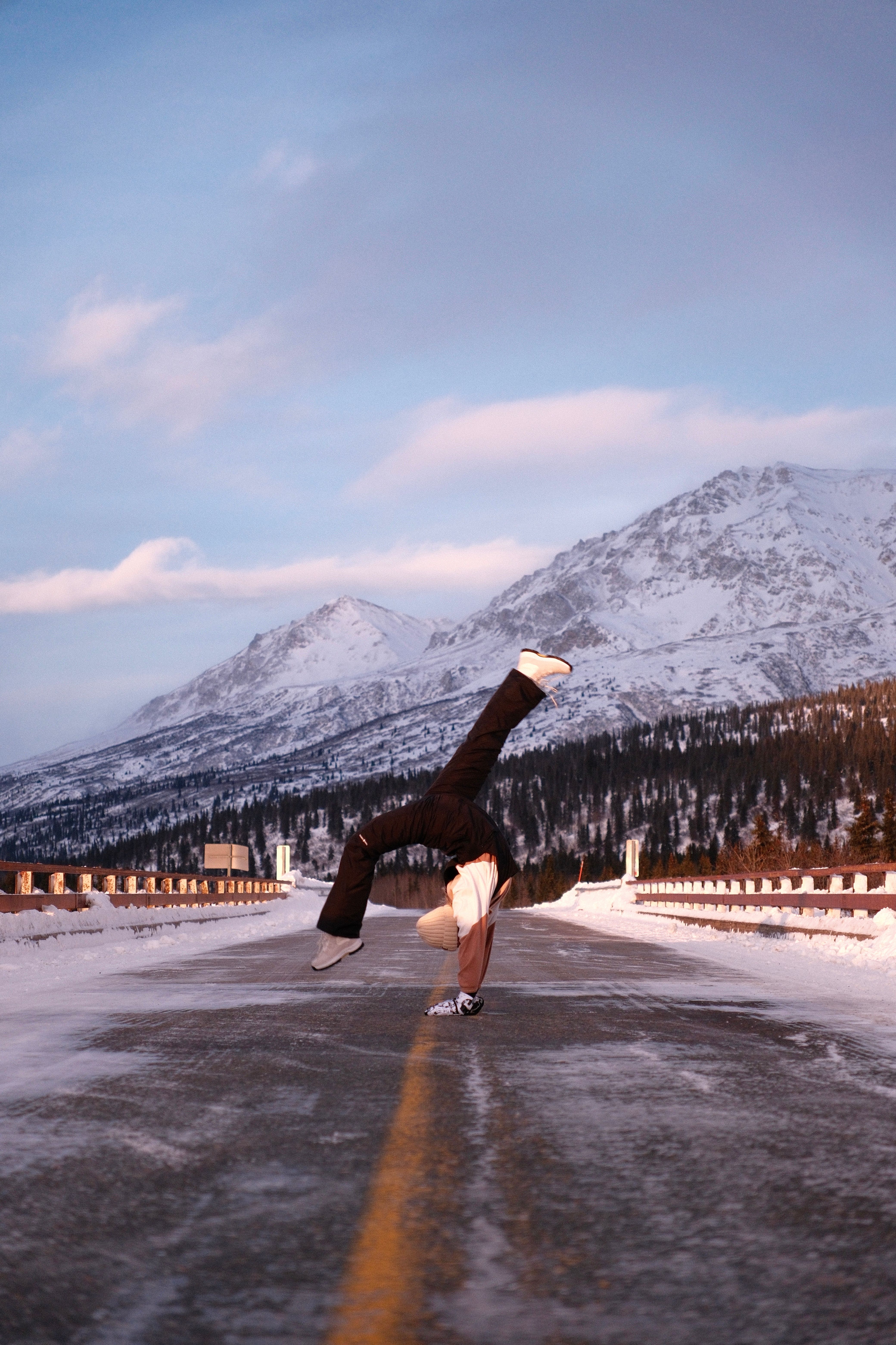 Dynamic breakdancer doing a flip on a snowy road with mountains in the background.