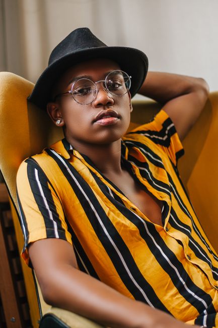 Trendy portrait of a man in a striking yellow and black striped shirt with a fedora and glasses.