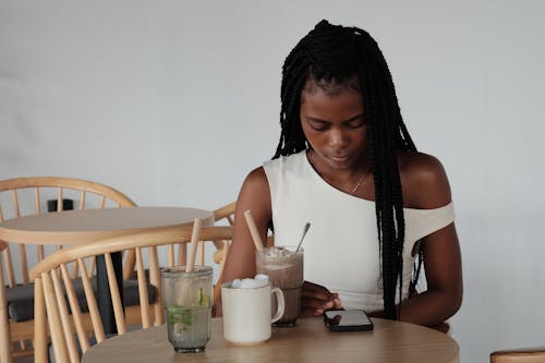 A woman sitting at a table with a phone and a drink